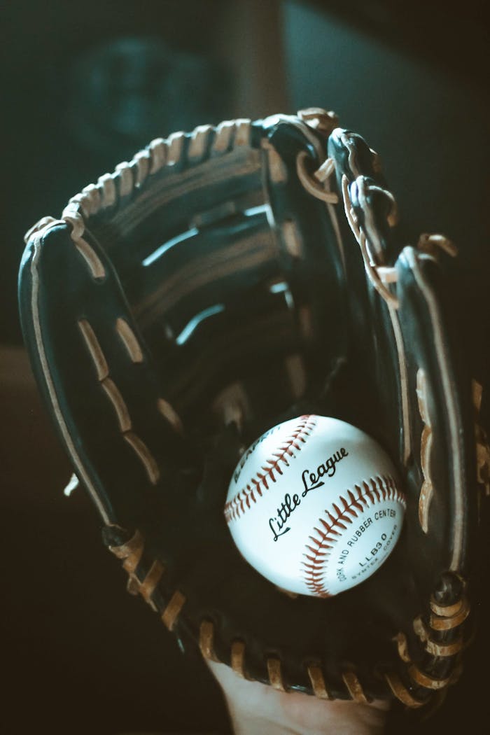 Close-up of a classic leather baseball glove holding a Little League ball, showcasing sports equipment details.