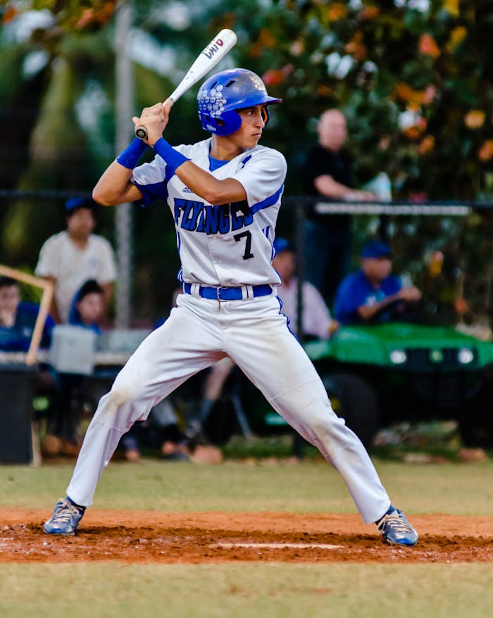our-story Teen baseball player in uniform ready to swing during a game on a grassy field.